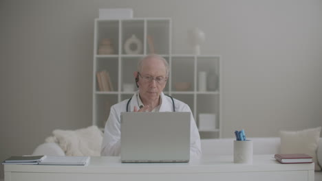 Un-Médico-Anciano-Trabaja-Remotamente-Desde-Su-Oficina-En-La-Clínica-Usando-Una-Computadora-Portátil-Para-Comunicarse-Con-Sus-Colegas